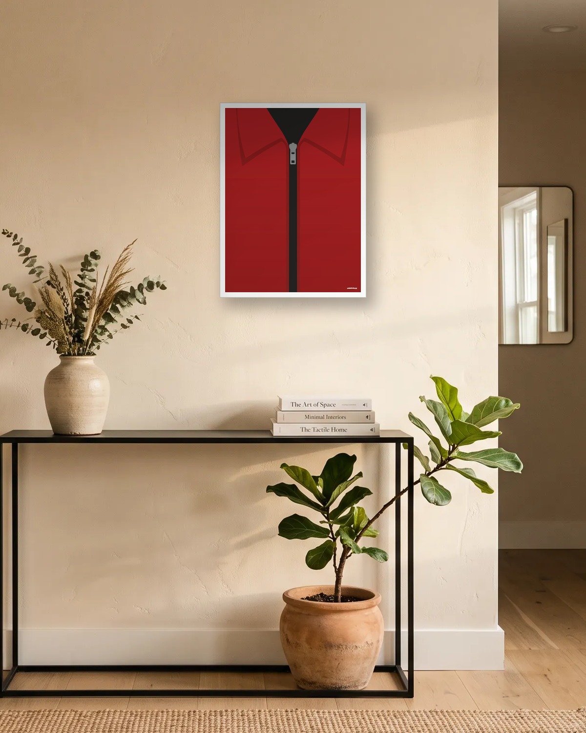 Affiche rouge minimaliste au-dessus d'une console noire dans une entrée claire : un col de combinaison rouge et un zip gris